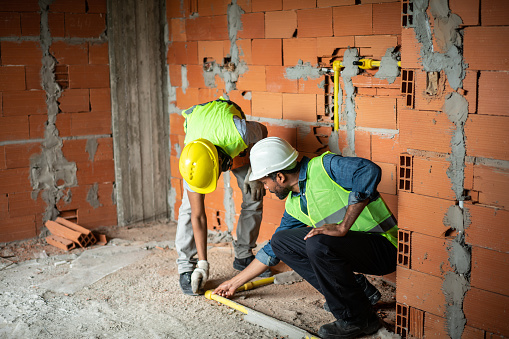 Two construction workers checking concealed pipe fittings of floor at a construction site. Building contractor with worker inspecting the site together.