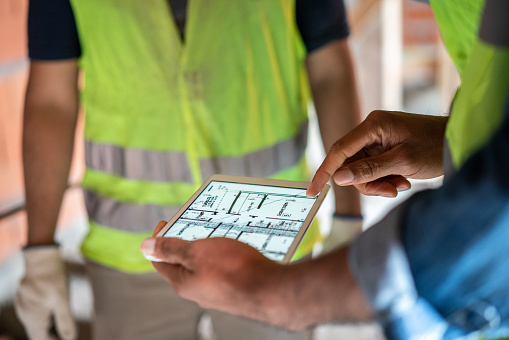 Construction site engineer reviewing blueprints on digital tablet