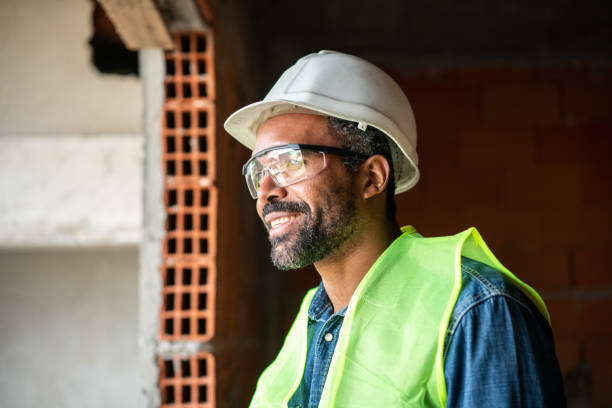 African man working at construction site Close-up of african man working at construction site. Mature male worker wearing work vest and safety hardhat standing at a new building site under construction. safety glasses stock pictures, royalty-free photos & images