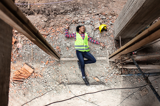 Top view of a woman worker fallen from the top elevation of scaffold on a construction site and landed on rubble at the base of the building. Construction worker accident lying unconscious on building site.