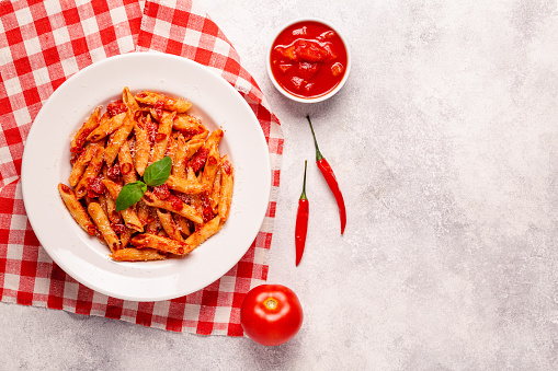 Classic italian pasta penne alla arrabiata with fresh basil on a light background, top view