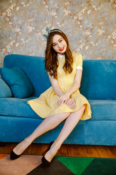 istock Cute young pin-up lady with red lipstick sitting on sofa 1352879651