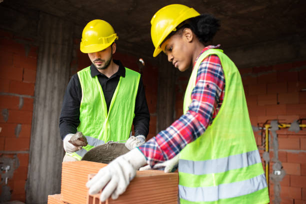 Two mason workers working at construction site Woman bricklayer building a wall with coworkers standing by and helping her at construction site. Two mason workers working at construction site. mason craftsperson stock pictures, royalty-free photos & images
