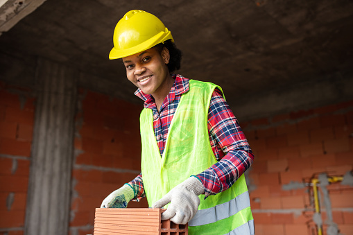 Portrait of a young woman bricklayer building a wall at construction site. Female mason worker working at construction site.