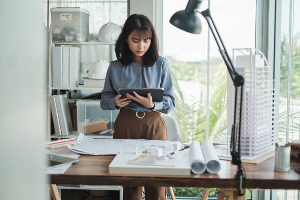 istock Portrait Asian woman Architect using tablet with blueprint and building model in office. 1352882292