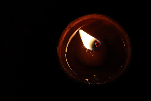 Stock photo showing elevated view of lit diya (oil lamp), with flickering flame in the dark, part of Diwali festival of lights celebration.