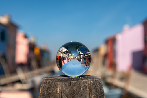 Glass ball lying on pillar in front of colorful houses in Burano, Venice (Italy), sunny day in late autumn
