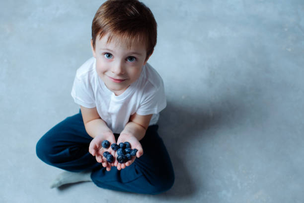 portrait of innocent smiling nice boy with blueberries in his hands. health and clean nutrition concept stock photo