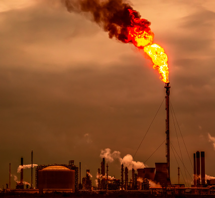 Air pollution from a large flame producing black smoke at a petrochemical plant at twilight.