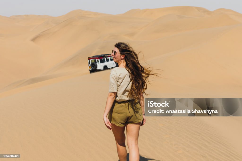 Woman traveler enjoying a day at the sand dunes by the sea with 4X4 car in Namibia Young woman with long hair in sunglasses walking to her old truck car during the windy day at the sand dunes of Sandwich Harbour in Namib-Naukluft National park, Namibia, Souther Africa 4x4 Stock Photo
