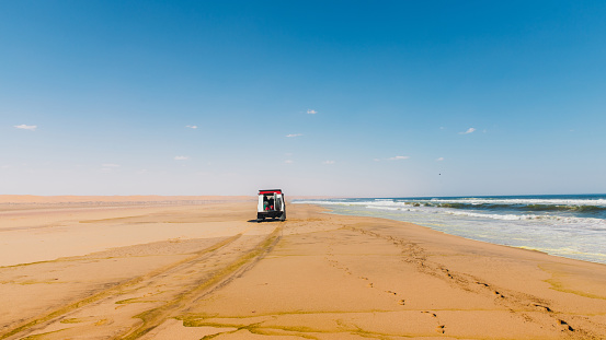 Scenic view of the off-road car driving the sand beach at the Atlantic Ocean in Namib-Naukluft National park, Namibia