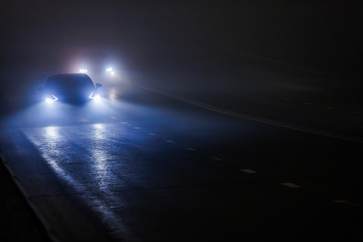 two blurred cars moving on empty night foggy road.