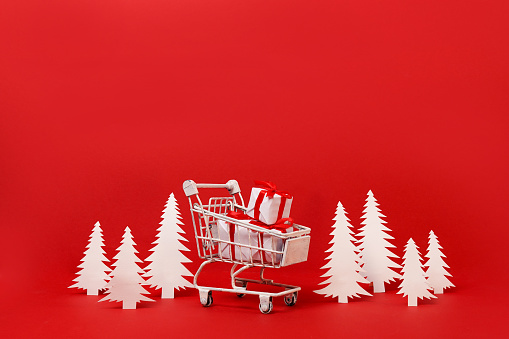 Shopping cart with Christmas gifts on red background. copy space