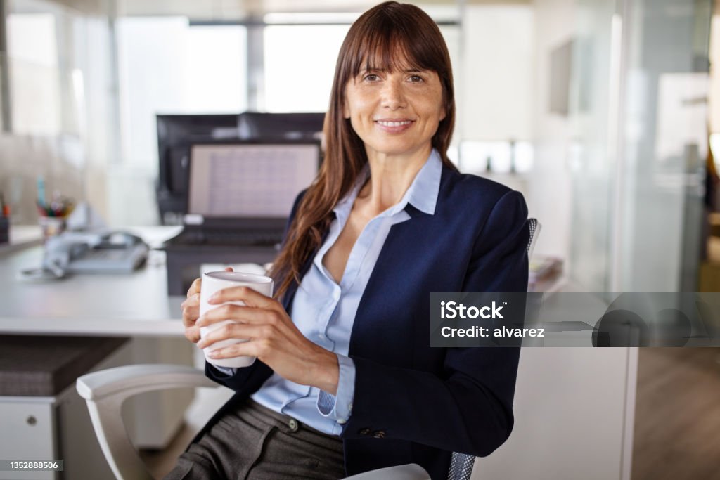 Portrait of a business woman having a coffee break in office Portrait of a female business executive looking at camera and smiling. Businesswoman having coffee break in office. Creative Director Stock Photo