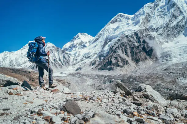 Young hiker backpacker female taking brake in hike walking enjoying Khumbu Glacier. High altitude Everest Base Camp route near Gorakshep,Nepal. Nuptse 7861m on background. Active vacations concept