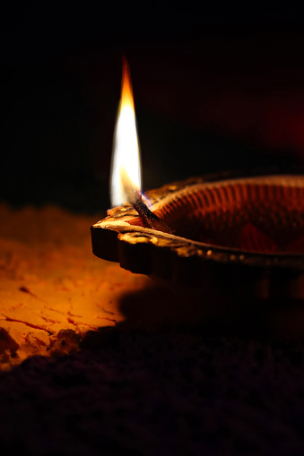Stock photo showing close-up view of lit diya (oil lamp), with flickering flame in the dark, part of Diwali festival of lights celebration.