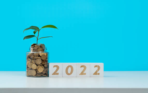 istock Coin jar and number 2022 on white table 1352893101