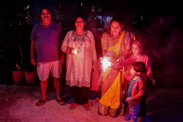 nahaufnahme der indischen hindu-familie, die diwali feiert, hinduistisches lichterfest mit wunderkerzen und feuerwerk, großvater, großmutter, schwiegertochter und enkelinnen, die lässige und traditionelle kleidung tragen - hinduism outdoors horizontal close up stock-fotos und bilder