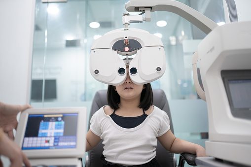 Asian Chinese girl sitting on chair doing eye test on digital Phoropter in ophthalmology clinic