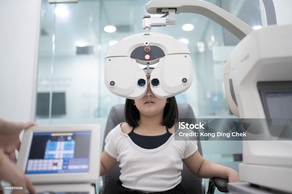 Asian Chinese girl sitting on chair doing eye test on digital Phoropter in ophthalmology clinic Eye Exam Stock Photo