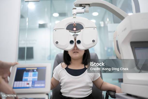 Asian Chinese Girl Sitting On Chair Doing Eye Test On Digital Phoropter In Ophthalmology Clinic Stock Photo - Download Image Now