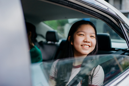 Image of an Asian Chinese teenage girl sitting in car back seat going for a road trip