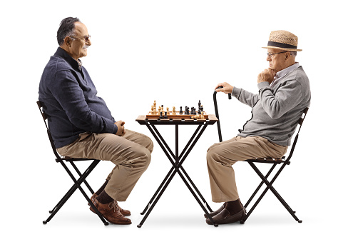 Two male pensioners playing chess at a table isolated on white background