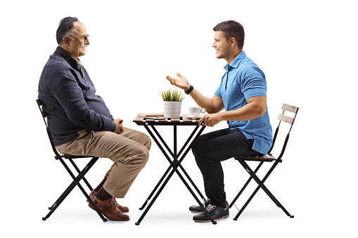 Young man sitting at a cafe and talking to a mature man isolated on white background