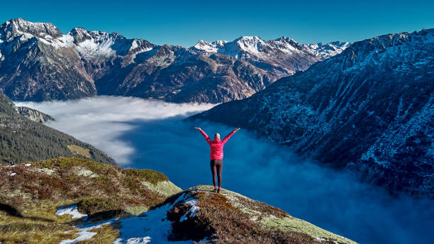 istock Hiker stands on mountain ridge above foggy valley 1352906421