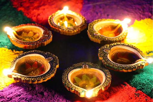 Stock photo showing a close-up view of flickering flames of oil filled diyas illuminating gulal rangoli design to celebrate Diwali the festival of lights.