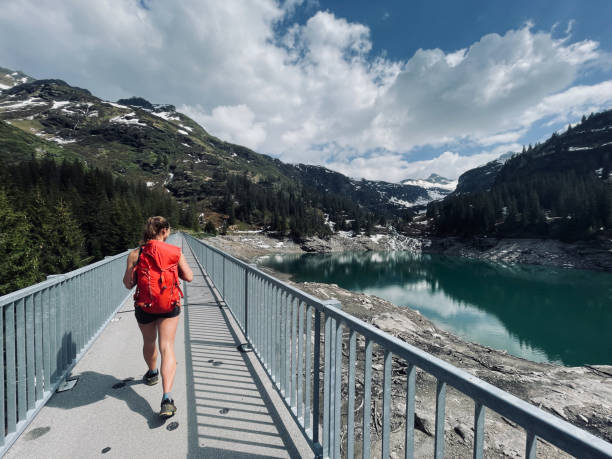 istock Backpacker hikes along bridge over mountain shoreline 1352906569