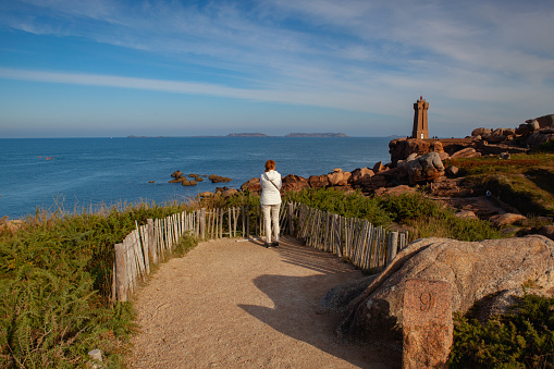 Ploumanach, France - 17 October, 2021: Lonely women on the Pink Granite Coast. Pink Granite Coast is a stretch of coastline in the Cotes d Armor departement of northern Brittany, France. It stretches for more than thirty kilometres.