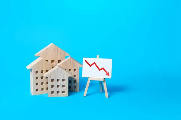 Photo of Residential buildings and down arrow graph on easel. Low property value, low price. Real estate market fall. Lower mortgage interest rates. Falling prices for rental. Affordable housing. Crisis