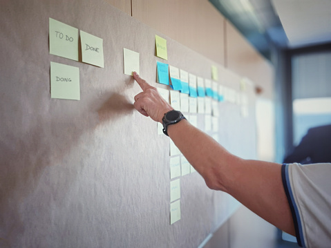 IT worker tracking his tasks on kanban board. Using task control of agile development methodology. Man pointing a blank sticky note to scrum task board in the office stock