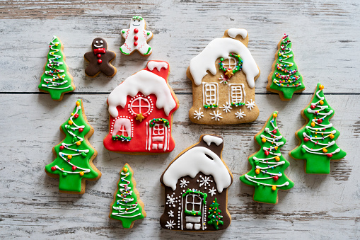 Three gingerbread houses surrounded by gingerbread Christmas trees and two gingerbread men all decorated with icing against a backdrop of a wooden tabletop