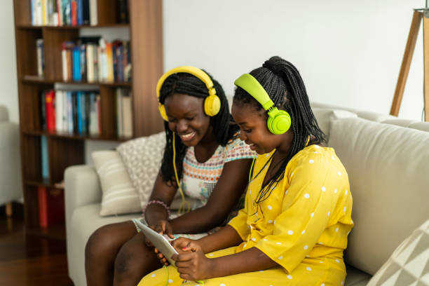 две счастливые молодые женщины, подстраивающиеся под музыку через интернет - sofa music teenager friendship стоковые фото и изображения