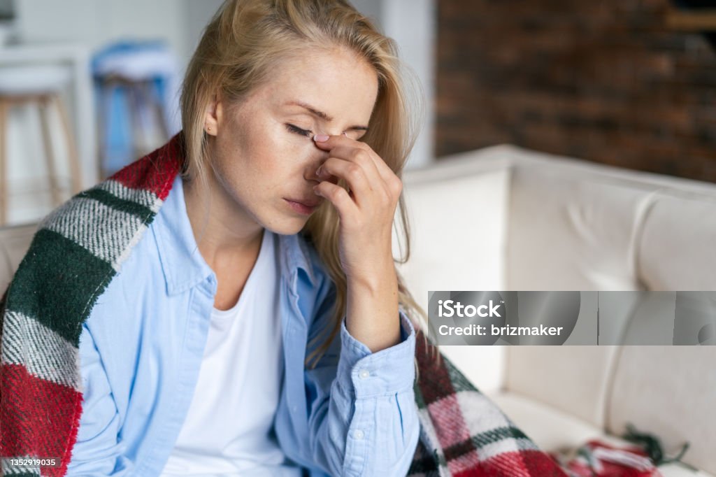 Tired woman with closed eyes touching nose bridge Fatigue and upset woman touching nose bridge feeling eye strain or headache, trying to relieve pain. Sick and exhausted female spending day at home. Depressed lady feeling weary dizzy Tired Stock Photo