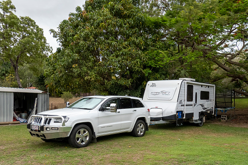 Townsville, Queensland, Australia - November 2021: A car and caravan parked in the shade of a large spreading tree beside a shed