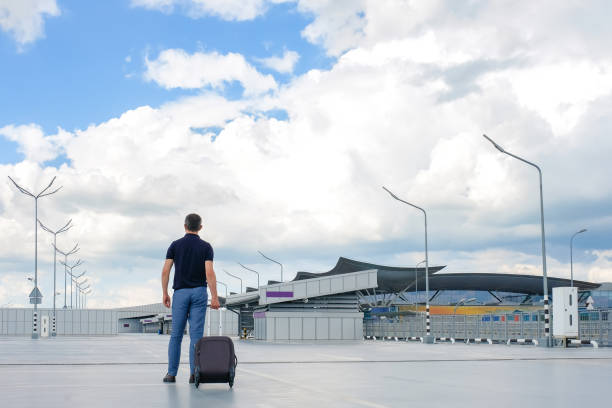 istock A young man with a suitcase in his hands in an open empty parking lot. Back view, Vacation concept 1352926653