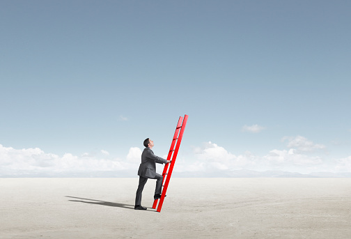 A businessman leans a ladder as though he is going to climb it but he has nothing to lean it against.