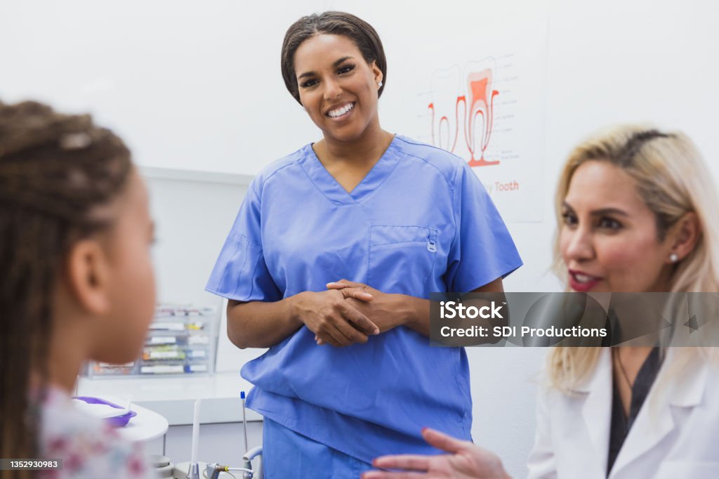 Pediatric dentists talks about girl's dental health An attentive little girl listens as a female pediatric dentist discusses the importance of brushing and flossing. Dental Assistant Stock Photo