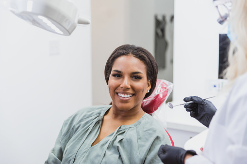A confident female dental patient smiles at the camera during a dental appointment.
