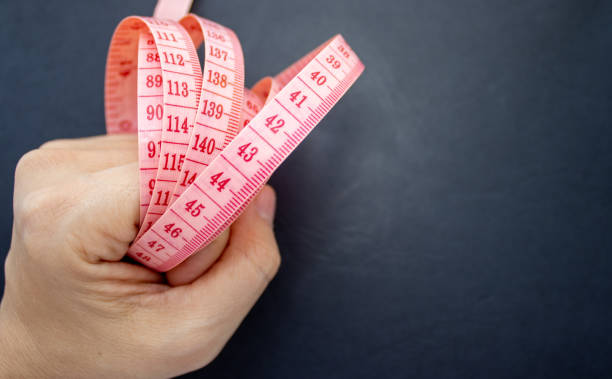 istock pink measure tape on black background in a woman's hand. 1352932248