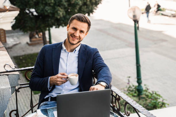 istock Handsome man with cup of coffee is working online using laptop in cafe. Remote work. 1352933875