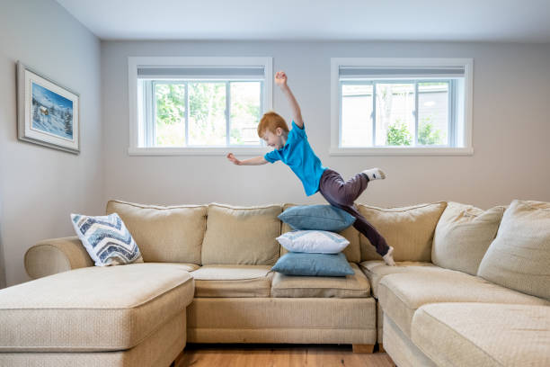 彼のリビングルームでソファの上のクッションを飛び越えるかわいい赤毛の少年 - domestic life jumping child sofa ストックフォトと画像