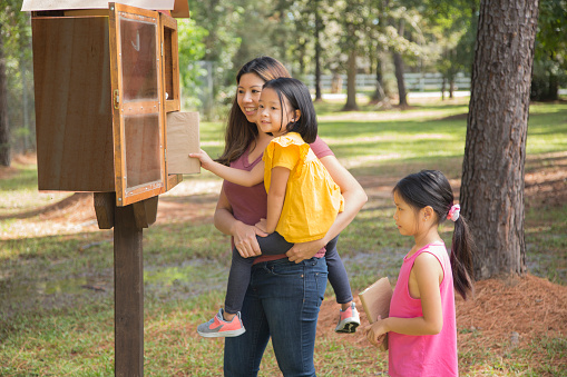 Estudiantes de preescolar y jardín de infantes en la caja de libros compartidos ubicada en el parque comunitario.  Niñas de preescolar y jardín de infantes. photo