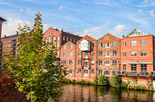 Row of old brick warehouses converted in lofts along a river on a sunny autumn day. Leeds, UK.