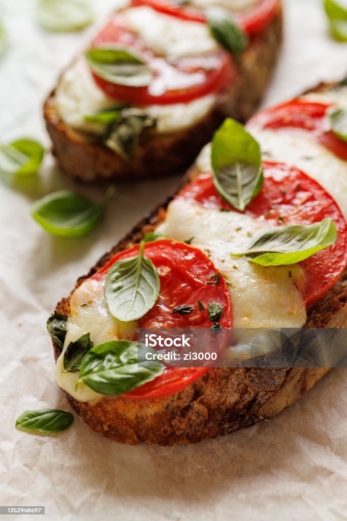 Grilled caprese sandwich based on sourdough bread with the addition of tomatoes, mozzarella cheese, fresh basil and olive oil Grilled caprese sandwich based on sourdough bread with the addition of tomatoes, mozzarella cheese, fresh basil and olive oil on a light background close up view Open Faced Sandwich Stock Photo