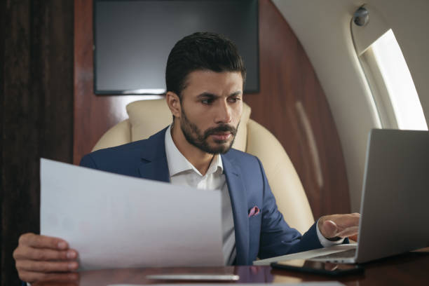 ближневосточный бизнесмен использует ноутбук, проводя финансовый отчет, работает с документами, сидящими в самолете. уверенный предприним - проводя поиск стоковые фото и изображения