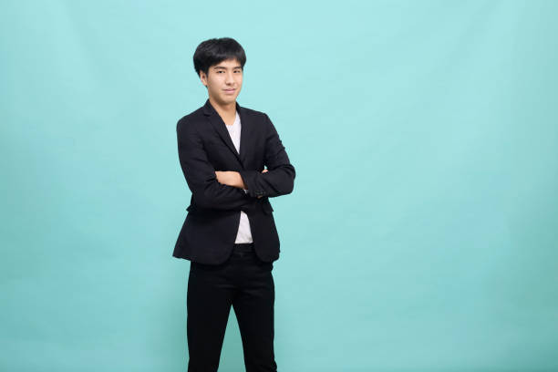 istock Handsome Asian man in a black suit arm crossed on light blue studio background 1352958719